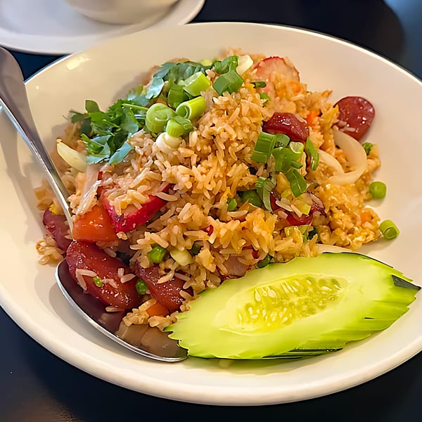 Thai fried rice with red pork, green onions, and a cucumber slice on a white plate.