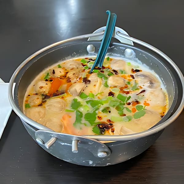 Creamy Thai soup with meatballs, mushrooms, and green onions in a metal pot with a serving spoon.