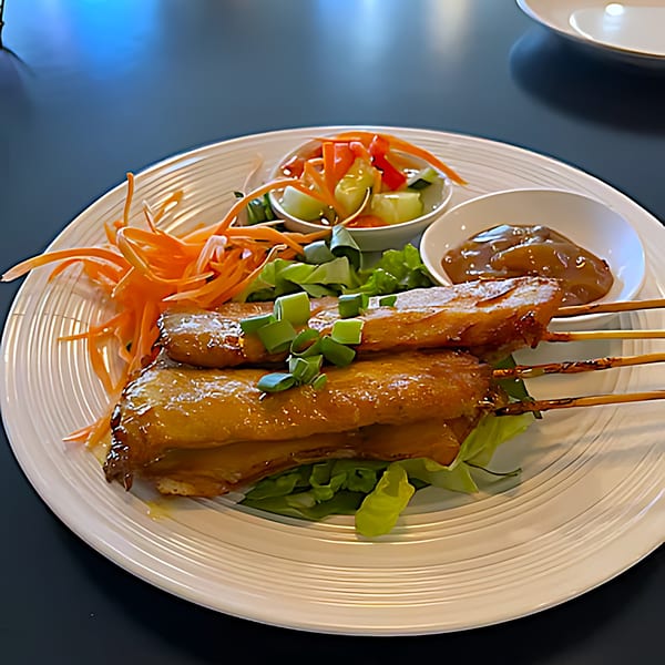 Thai chicken satay skewers with peanut sauce, pickled vegetables, and shredded carrots on a white plate.