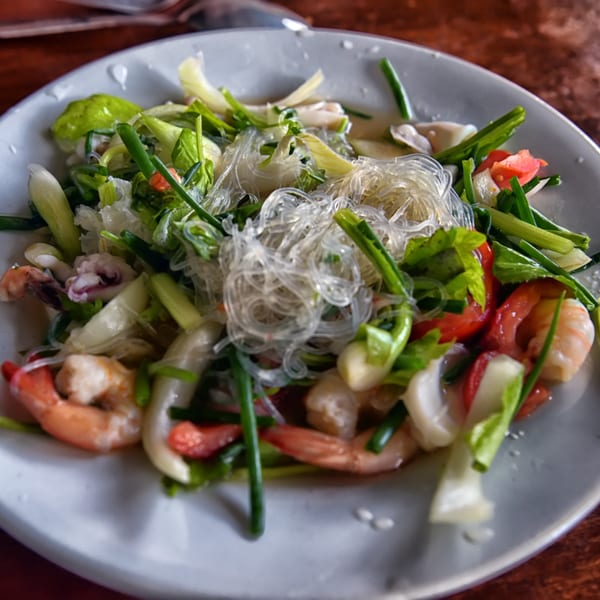 Thai glass noodle salad with shrimp, squid, green onions, and red peppers on a white plate.