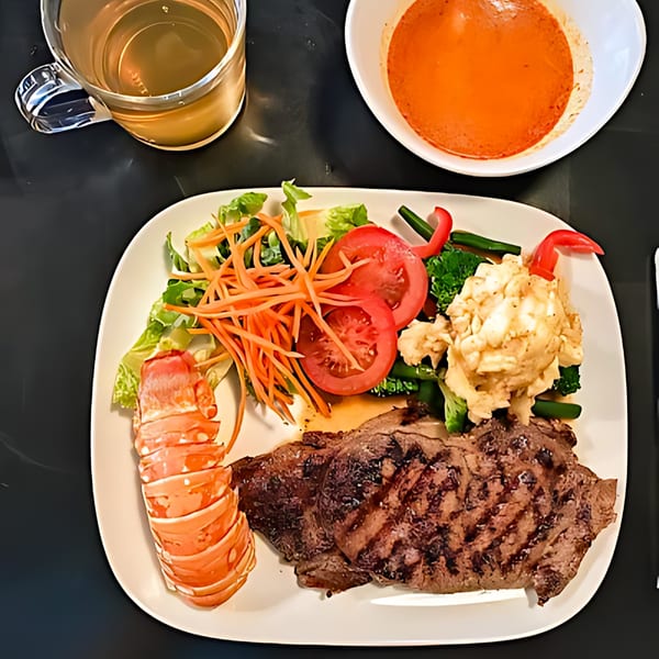 Grilled steak and lobster tail with a side salad, mashed potatoes, and a bowl of soup.