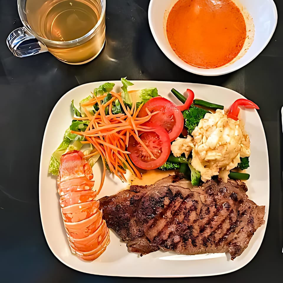 Grilled steak and lobster tail with a side salad, mashed potatoes, and a bowl of soup.